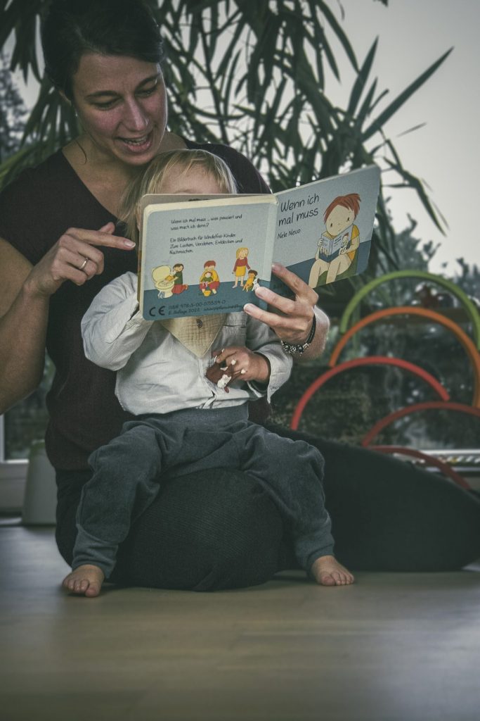 Mutter und Kind lesen das "Wenn ich mal muss" Buch. Kind trägt die Pfützenschutz Hose