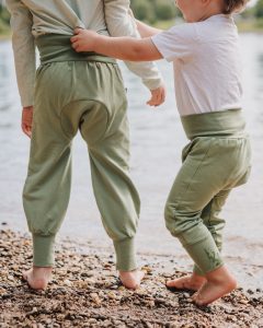 Zwei Kinder spielen am Flussrand und beide tragen die Windelweg Hose Auengrün, die sie beim Trockenwerden begleitet