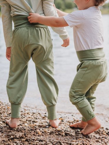 Zwei Kinder spielen am Flussrand und beide tragen die Windelweg Hose Auengrün, die sie beim Trockenwerden begleitet