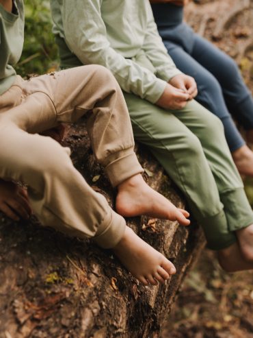 Drei Kinder mit Windelweg Hose sitzen nebeneinander auf einem Baumstamm