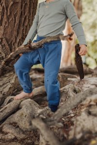 Kind spielt mit Ast und trägt eine Windelweg Hose in Flussblau als Sicherheit beim Trockenwerden
