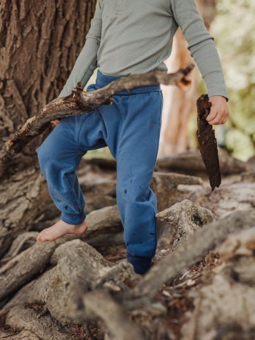 Kind spielt mit Ast und trägt eine Windelweg Hose in Flussblau als Sicherheit beim Trockenwerden